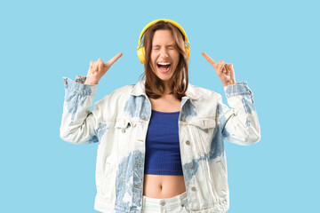 Happy young woman pointing at modern headphones while listening to music on blue background