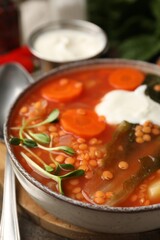 Tasty lentil soup with sour cream in bowl on table, closeup
