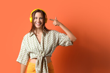 Happy young woman pointing at her modern headphones on orange background