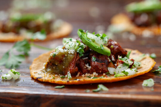 Close-up shot of a carne asada taco with onions, avocado, and cilantro on a corn tortilla, on a wooden table. 