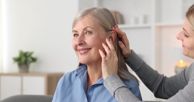 Woman putting hearing aid into her mother's ear at home, closeup