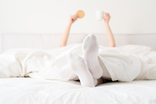 Female feet wearing white socks under blanket in bed. Woman waking up in the morning