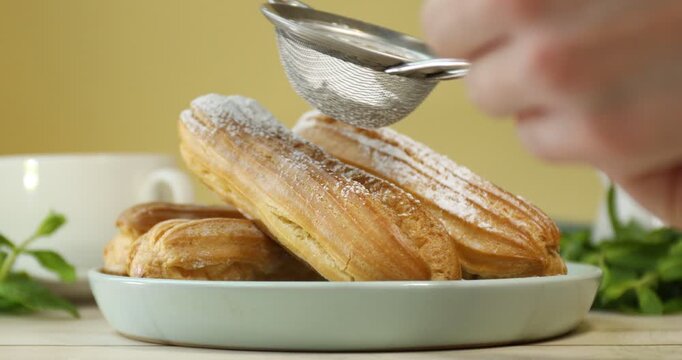Woman sprinkling eclairs with powdered sugar at white wooden table, closeup