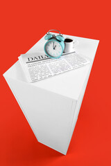 Alarm clock, coffee and newspaper on table against orange background