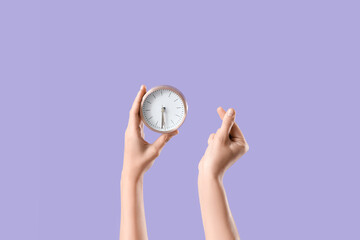 Female hands with alarm clock showing heart gesture on lilac background