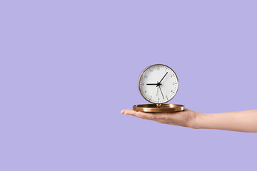 Female hand with alarm clock on lilac background