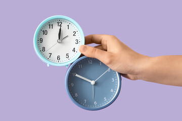 Female hand with alarm clocks on lilac background