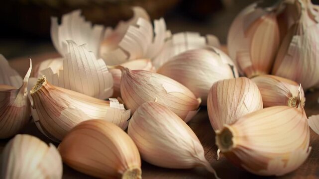 Pile of peeled and unpeeled garlic cloves with papery husks on wooden surface