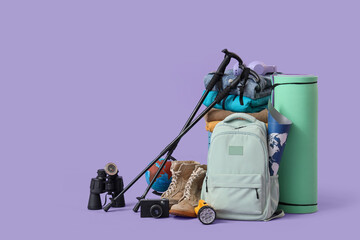 Walking poles, backpack and hiking equipment on lilac background