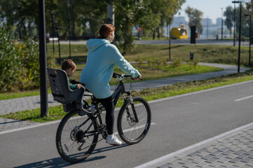 Caucasian woman rides bicycle with one-year-old son in park. 