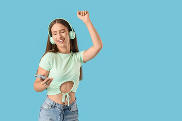 Beautiful young woman with modern mobile phone and headphones listening to music on blue background