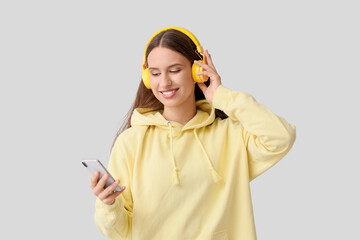 Beautiful young woman with modern mobile phone and headphones listening to music on grey background