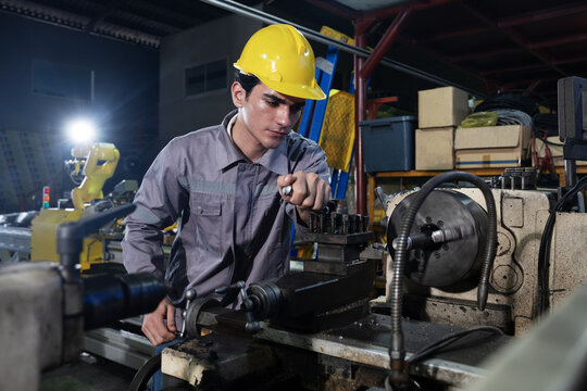 Young engineer working lathe machine precision metal machining in factory industrial workshop at night focused safety helmet tool control