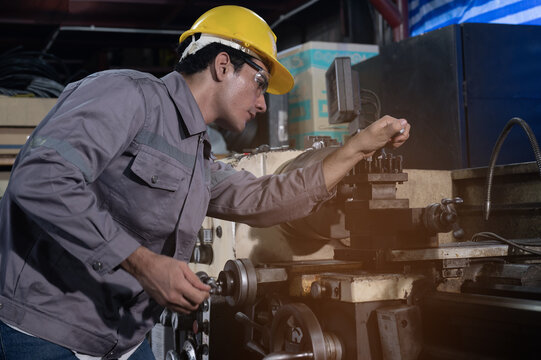 Industrial engineer adjusting metal lathe in factory workshop, focused engineers at work with safety helmet and goggles, industrial setting shows precision machine operation and calm concentration
