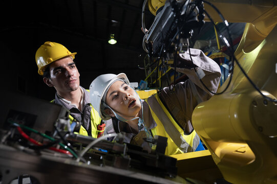 Industrial robot arm, factory floor, engineers inspect machinery with focused teamwork safety light, industrial control panel and metal gear visible, confident mood enhances precision workflow