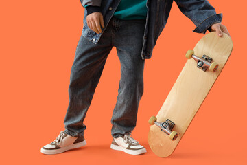 Legs of young man with skateboard on orange background, closeup © Pixel-Shot