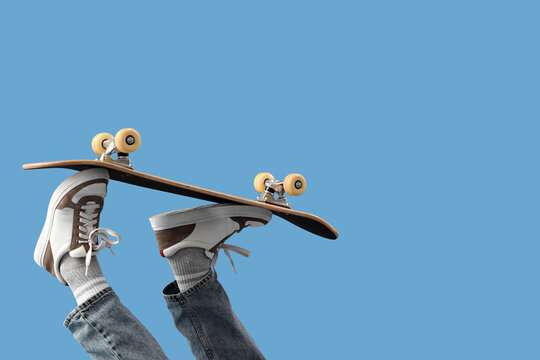 Legs of young man with skateboard on blue background, closeup