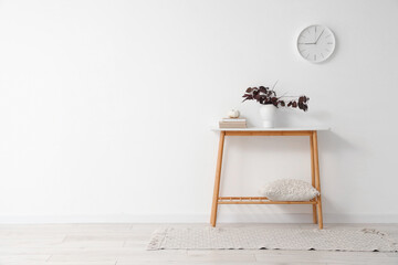 Vase with autumn leaves, pumpkin and books on table near light wall in room