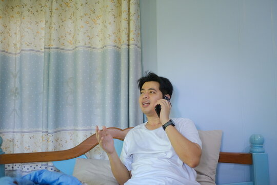 A man is talking on his cell phone while sitting on a bed