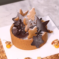 Delicious chocolate tart decorated with star and leaf cookies, walnuts, and cape gooseberries on a marble background. Perfect for holiday dessert, bakery presentation, or festive food photography