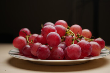 Juicy red grapes sit neatly on a plate in soft lighting