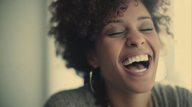 A young Black woman with curly hair laughs heartily with closed eyes showing her teeth - Powered by Adobe