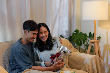 Happy young couple show love at home, woman receives romantic valentine day gift from man, sharing tender moment, celebrating special occasion with joyful smiles and affection, expressing happiness