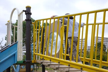 Rear View of a Child Crossing a Yellow Wooden Bridge in a Public Playground