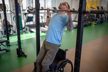 Resilient disabled man in wheelchair do pull up at gym to train upper body muscles. Accessible fitness for inclusive male, exercise strength, athlete workout, build shoulder and core power in gym