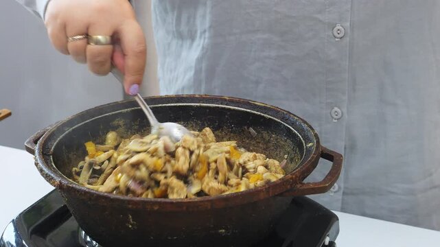 Chicken, onions, and champignons in teriyaki sauce are fried in a deep cast-iron skillet