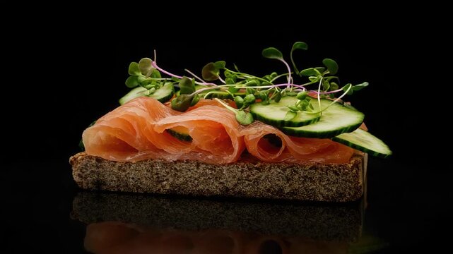 Smoked salmon slices on a slice of rye bread topped with cucumber, sprouts, seeds and purple onions