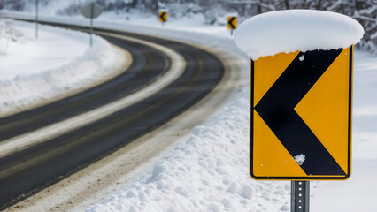 Curved road sign covered with snow – Symbol of winter road hazards