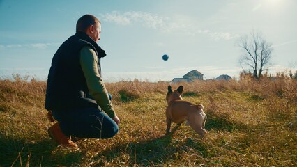 A Man Enjoying a Sunny Day Outdoors Playing Fetch with His Energetic Dog in a Natural Setting Surrounded by Open Fields and Clear Blue Skies