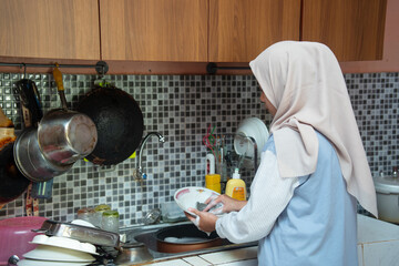 A woman washes dishes in the kitchen, cleaning tableware with soap and water as part of her daily household routine.