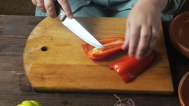 A woman's hands slice red peppers on a cutting board on the table