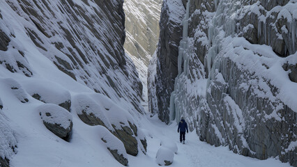 Hiker explores a picturesque snowy canyon with icy walls and deep snow, surrounded by serene wilderness. The scene captures the essence of adventure and solitude. Image made using Generative AI.