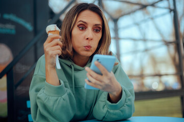 Surprised Woman Eating Ice Cream Reading Text Message. Shocked lady checking her mobile notifications while having dessert
