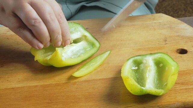 A woman's hands slice green peppers on a cutting board on the table