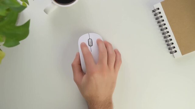 Hand on a Computer Mouse: A hand rests on a sleek, white computer mouse, poised for navigation. Next to it, a coffee cup and notebook signify the modern workspace.