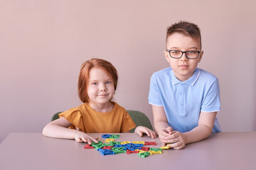 Caucasian children playing with colorful alphabet letters on table.