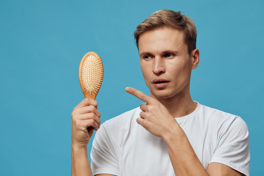 young caucasian man holding hairbrush pointing serious expression blue background casual white t-shirt digital detox concept