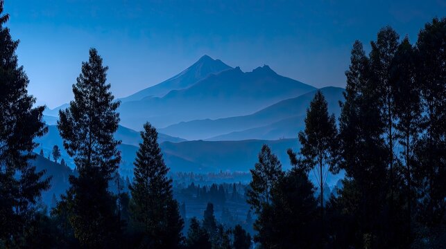Breathtaking mountain range shrouded in blue mist, framed by majestic trees, perfect for travel blogs, nature documentaries, and serene wall art