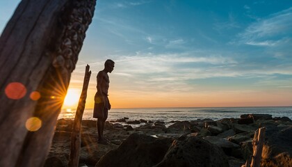 Silhouette of Man Standing on Rocky Beach at Sunset with Warm Colors and Dramatic Sky