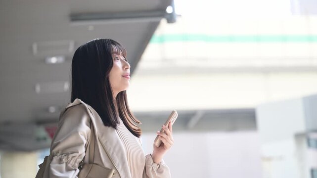 空港や交通機関のターミナルででスマホを持つ女性の写真　旅行や休日のイメージ横顔の動画　笑顔で歩く