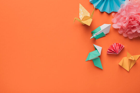 Vibrant origami creations and paper flowers adorn a bright orange background with copy space