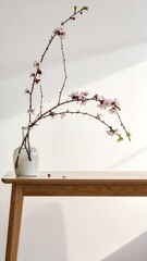 Delicate blooming branches in a vase on a light wooden table against a white wall