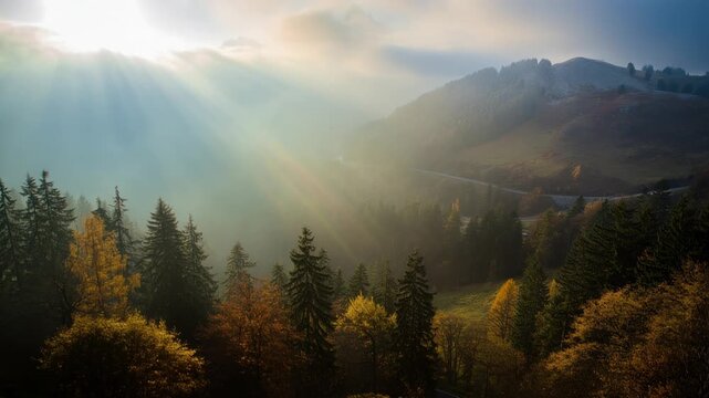 Morning sunbeams break through mist over a valley with a winding mountain road and autumn forest, wide angle descent revealing distant hills and tranquil fog
