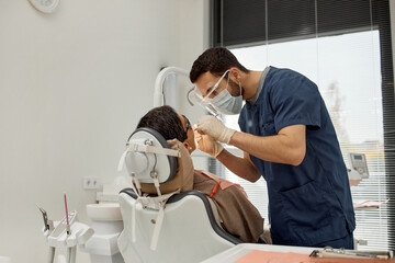 Young adult male dentist examining mature Caucasian woman sitting in dental chair during dental...