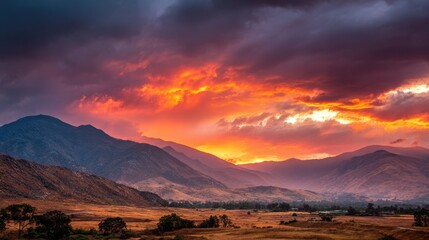 Breathtaking sunset scenery features vivid colors in the sky above a mountain range. The landscape includes valleys and hills creating a tranquil setting at dusk.