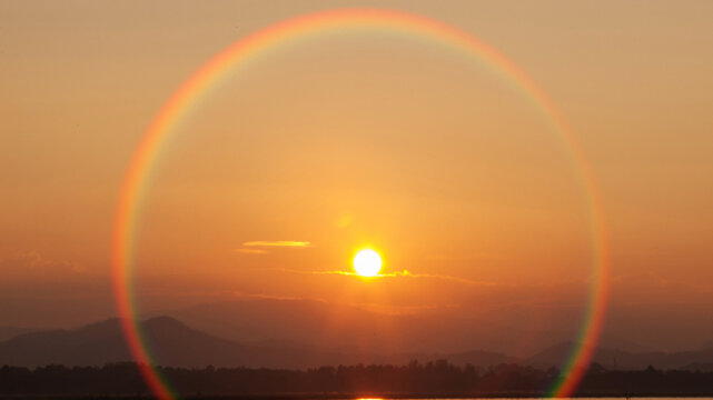 Full circular rainbow halo appearing around the sun during a golden sunset.